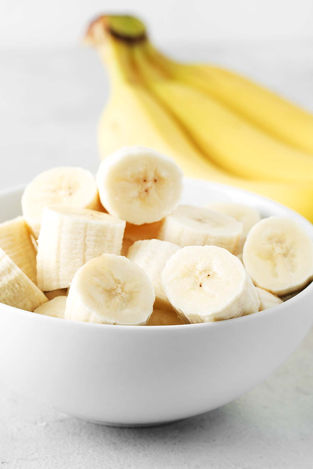 Sliced bananas in a white bowl with whole bananas in the background.