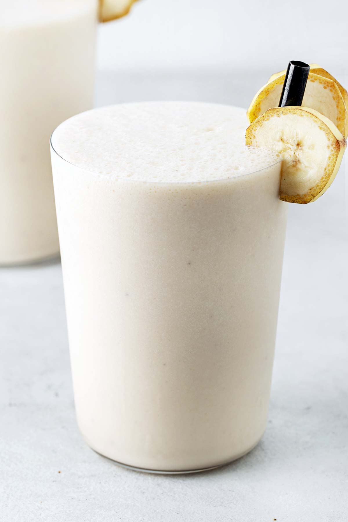 Banana milkshake in a glass with a black straw.