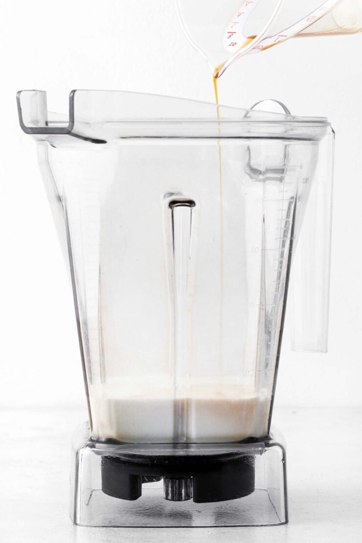 Pouring vanilla extract into a blender with milk.