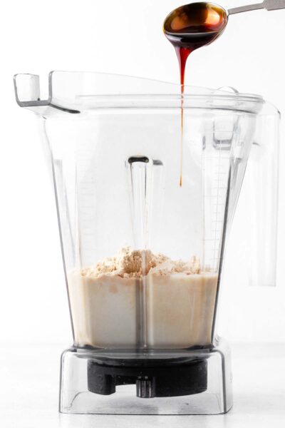 Date syrup being poured into a blender with oat milk and protein powder.