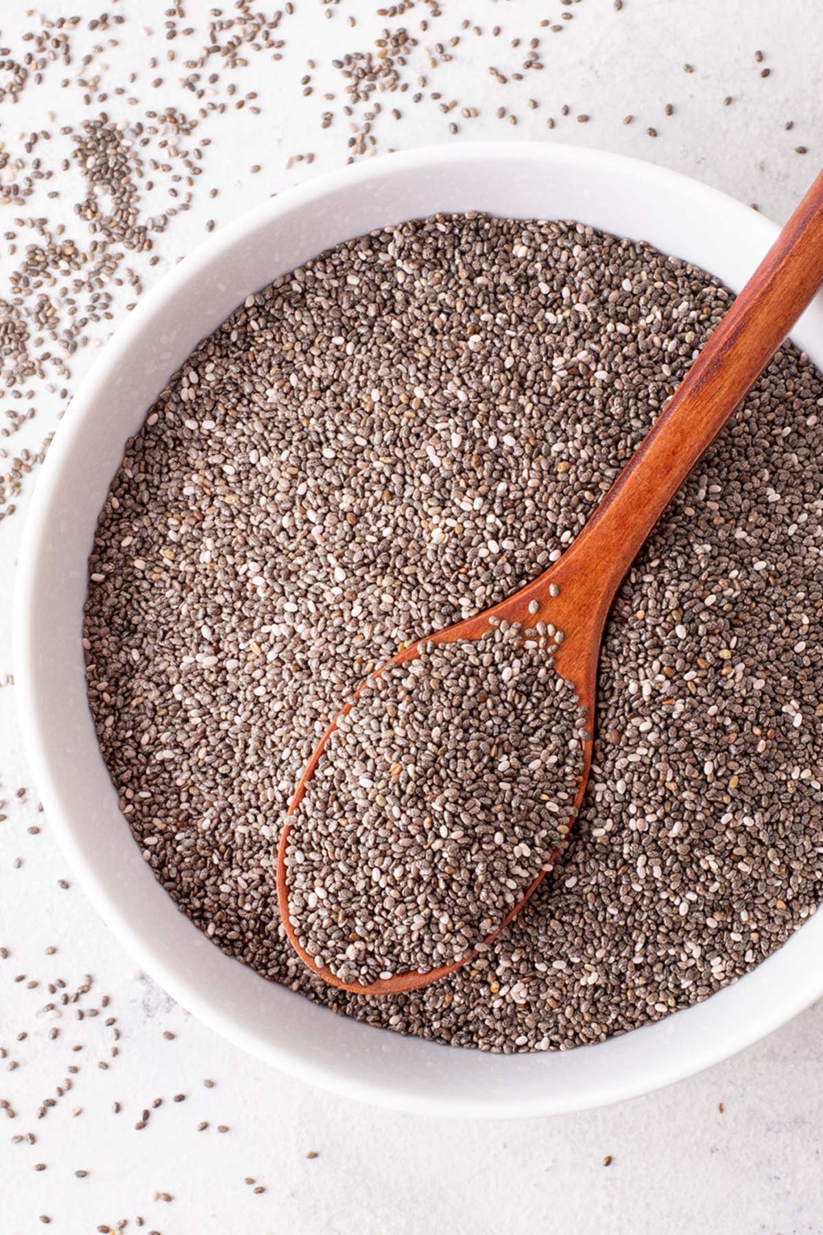 Chia seeds in a white bowl with a wooden spoon.