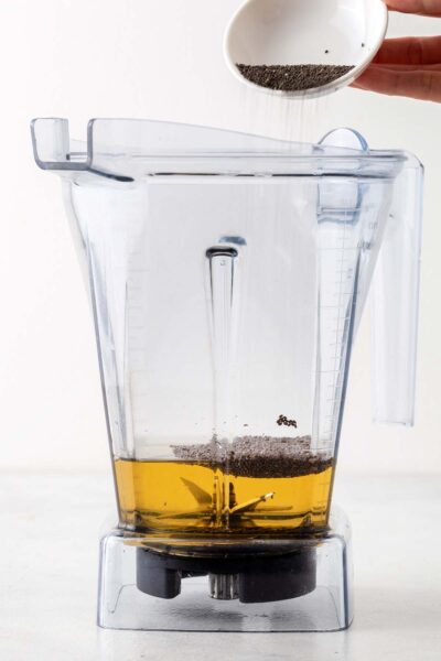 Chia seeds being poured into a blender with apple juice.
