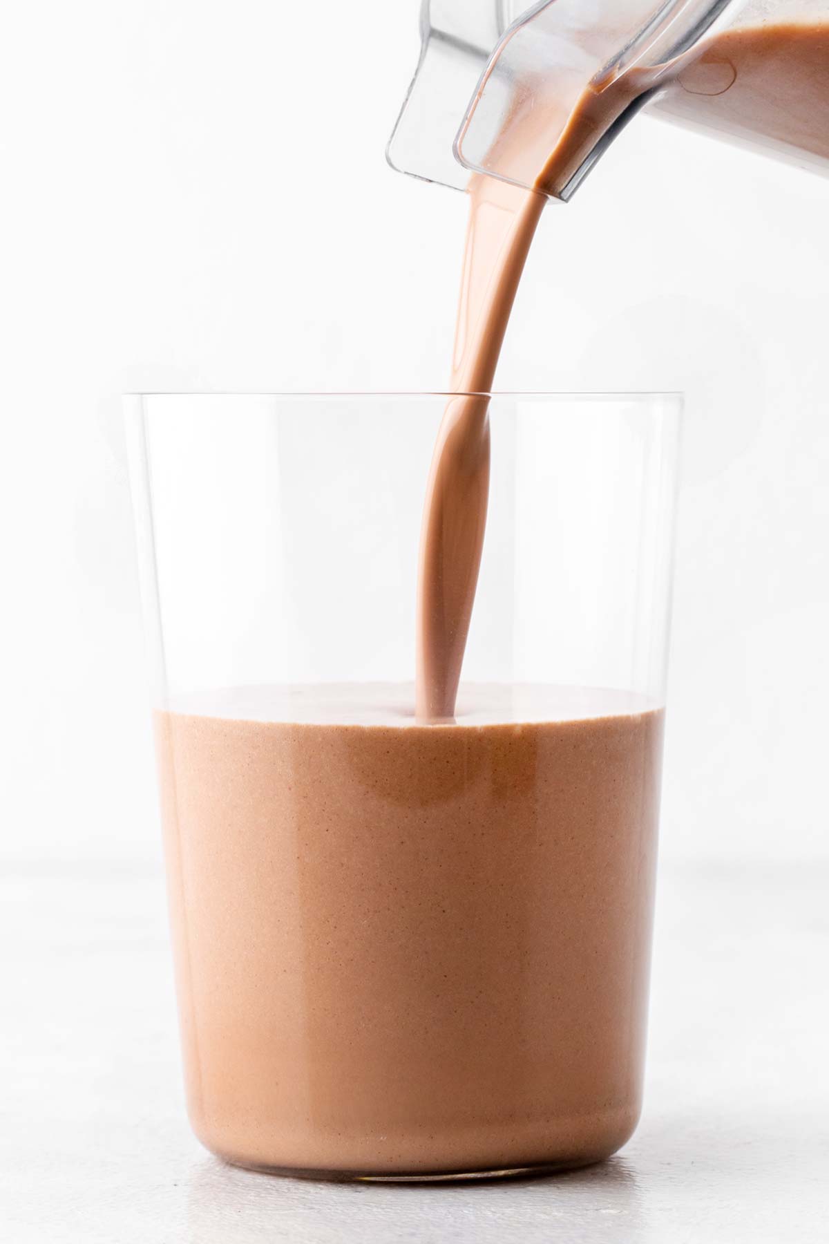 Pouring a chocolate almond protein shake in a glass.