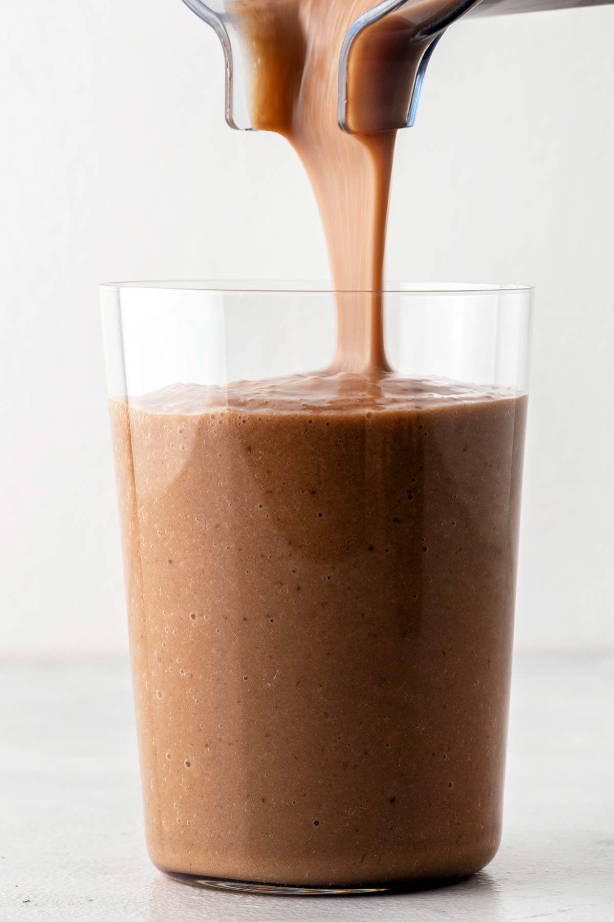 Pouring chocolate collagen smoothie in a glass.