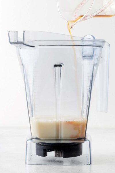 Vanilla extract being poured into a smoothie with milk. 
