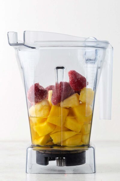 Strawberries, frozen pineapple, grape juice, and mango in a blender.