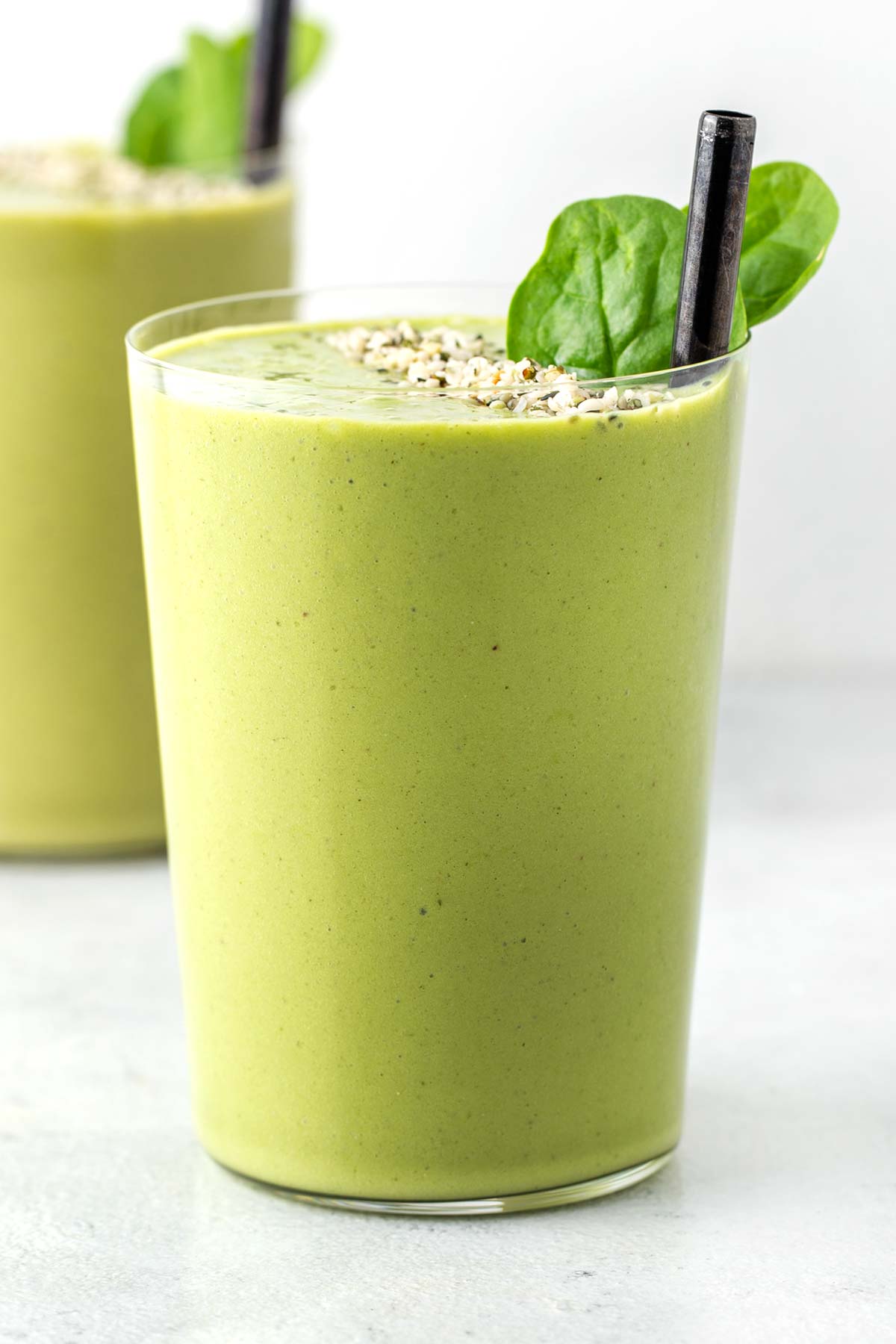 Green protein smoothies in cups with black straws.