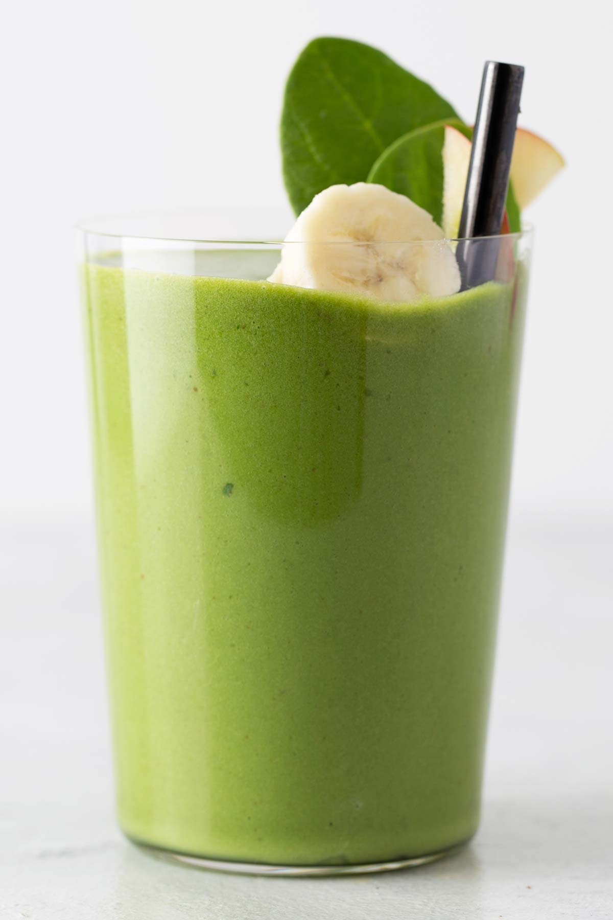 Green smoothie in a cup topped with fresh fruit garnishes.