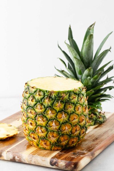Pineapple on a wooden cutting board with the top and bottom cut off.