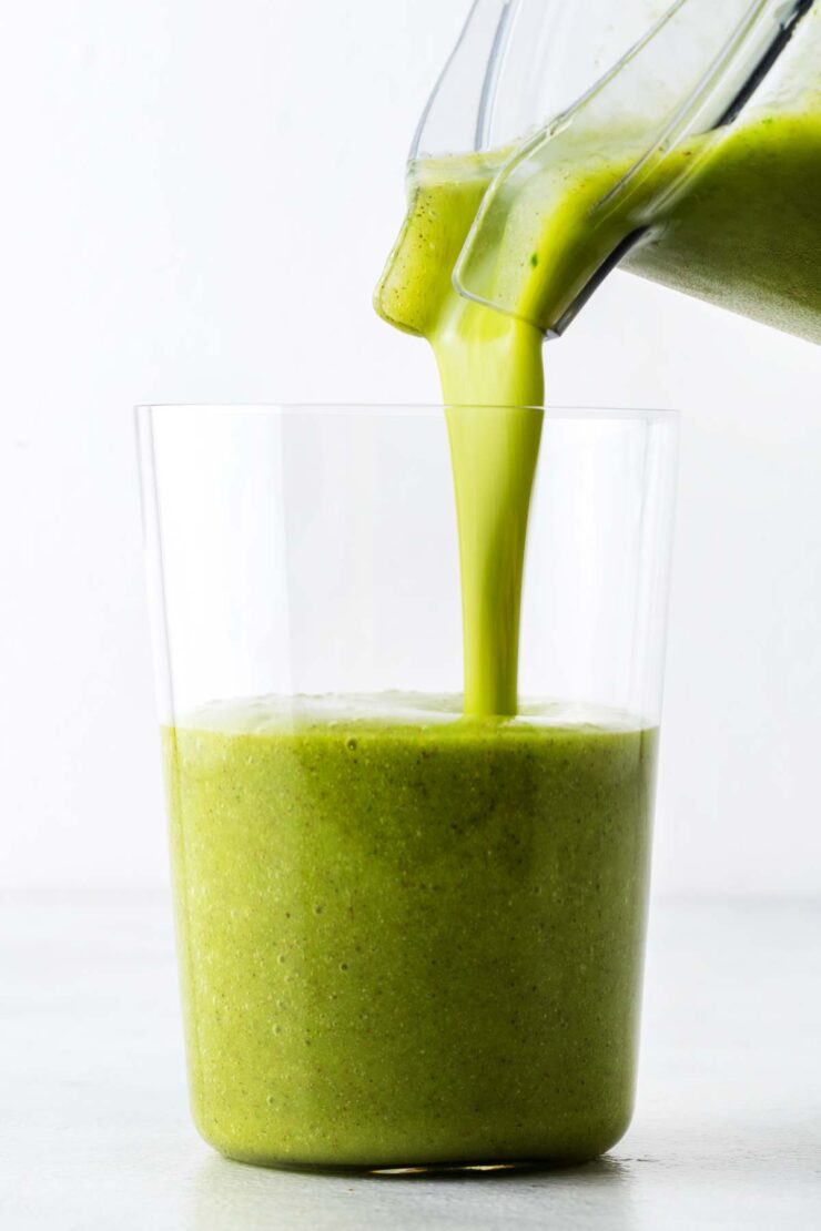 Pouring a green smoothie into a blender.