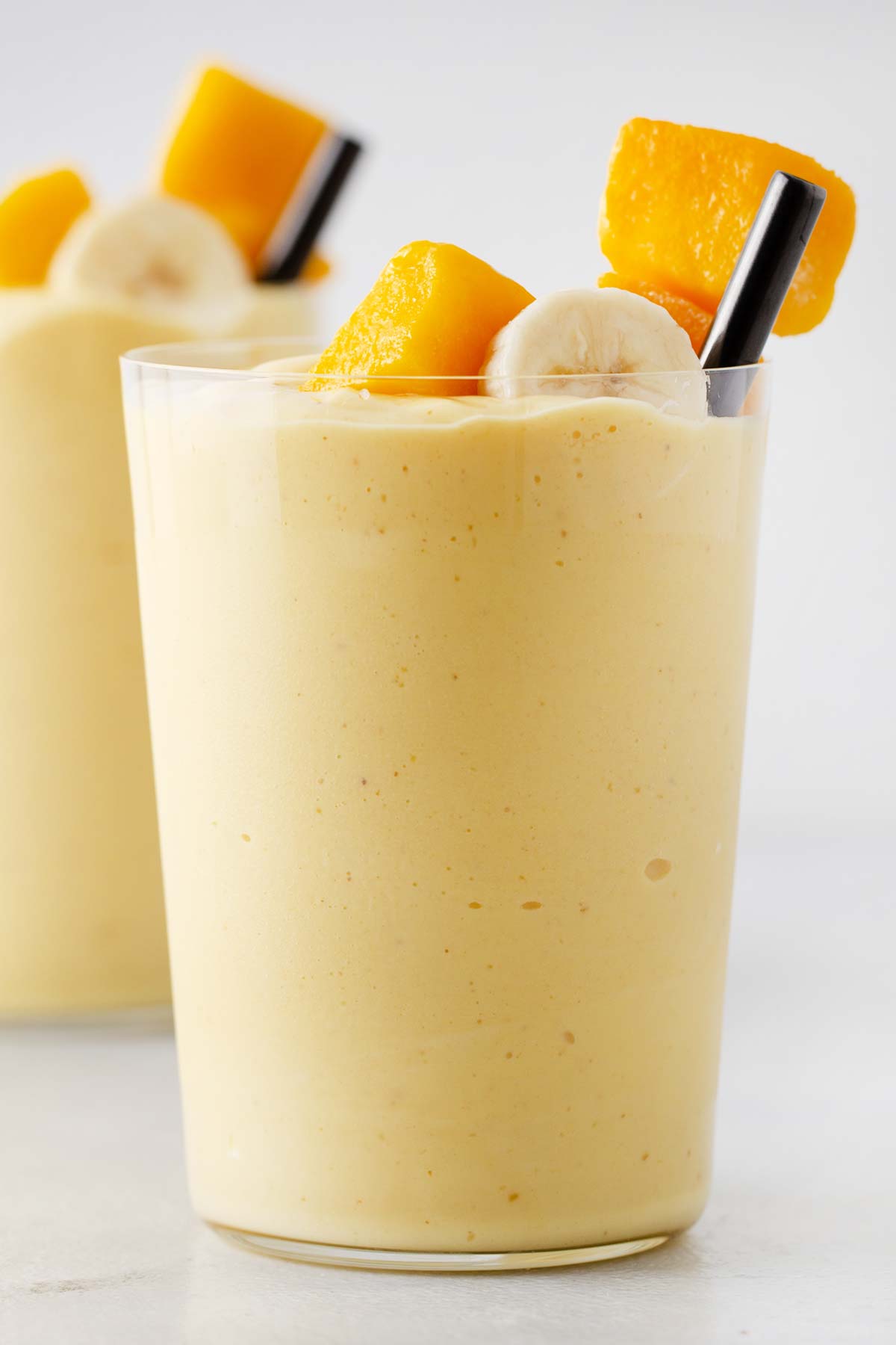 Mango yogurt smoothie in a glass cup with a metal straw.