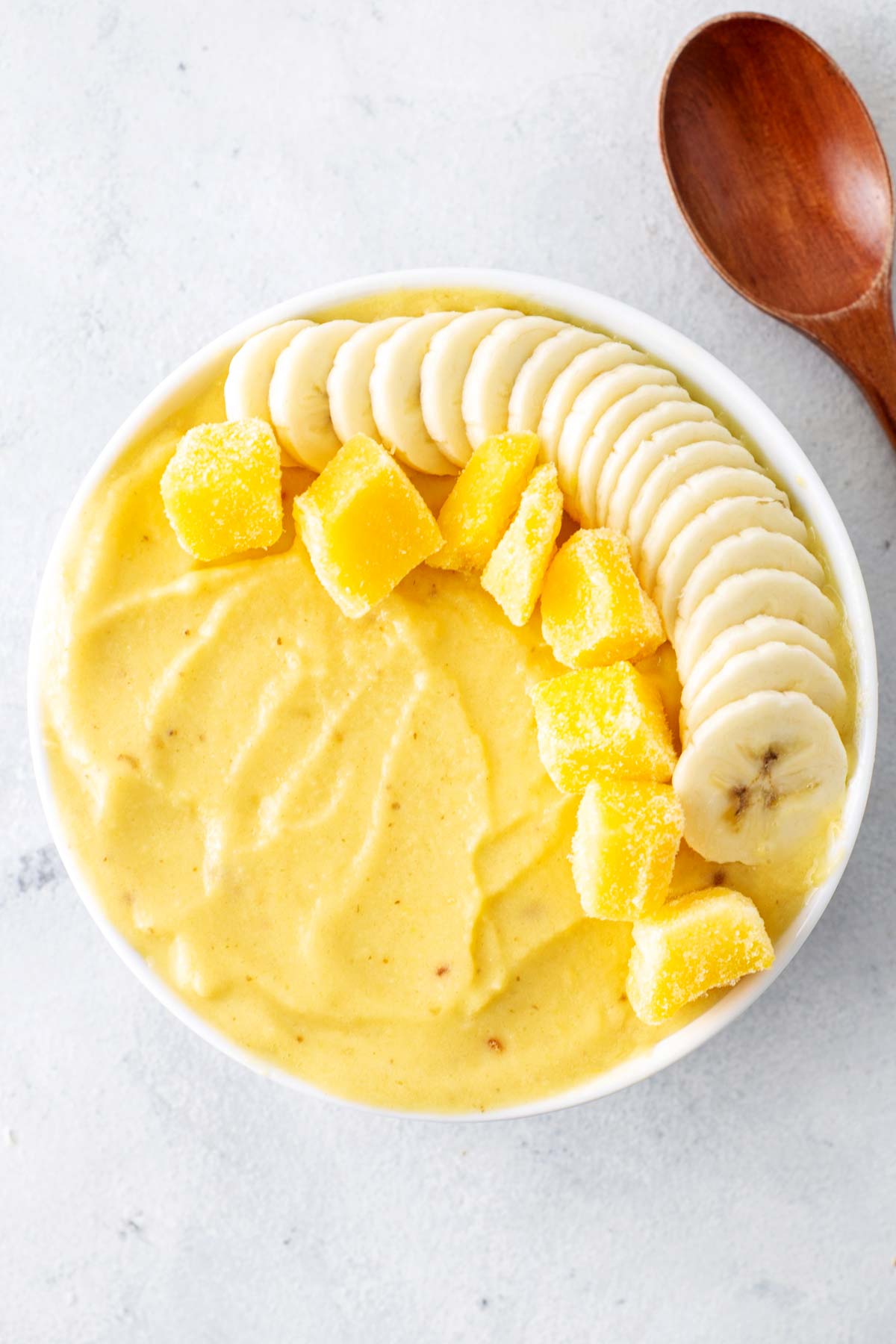 Mango smoothie bowl with a wooden spoon off to the side.