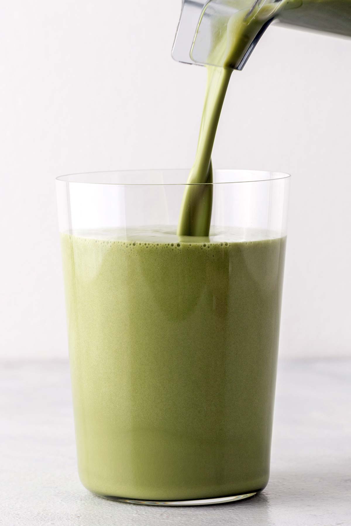 Pouring a matcha protein shake into a glass.