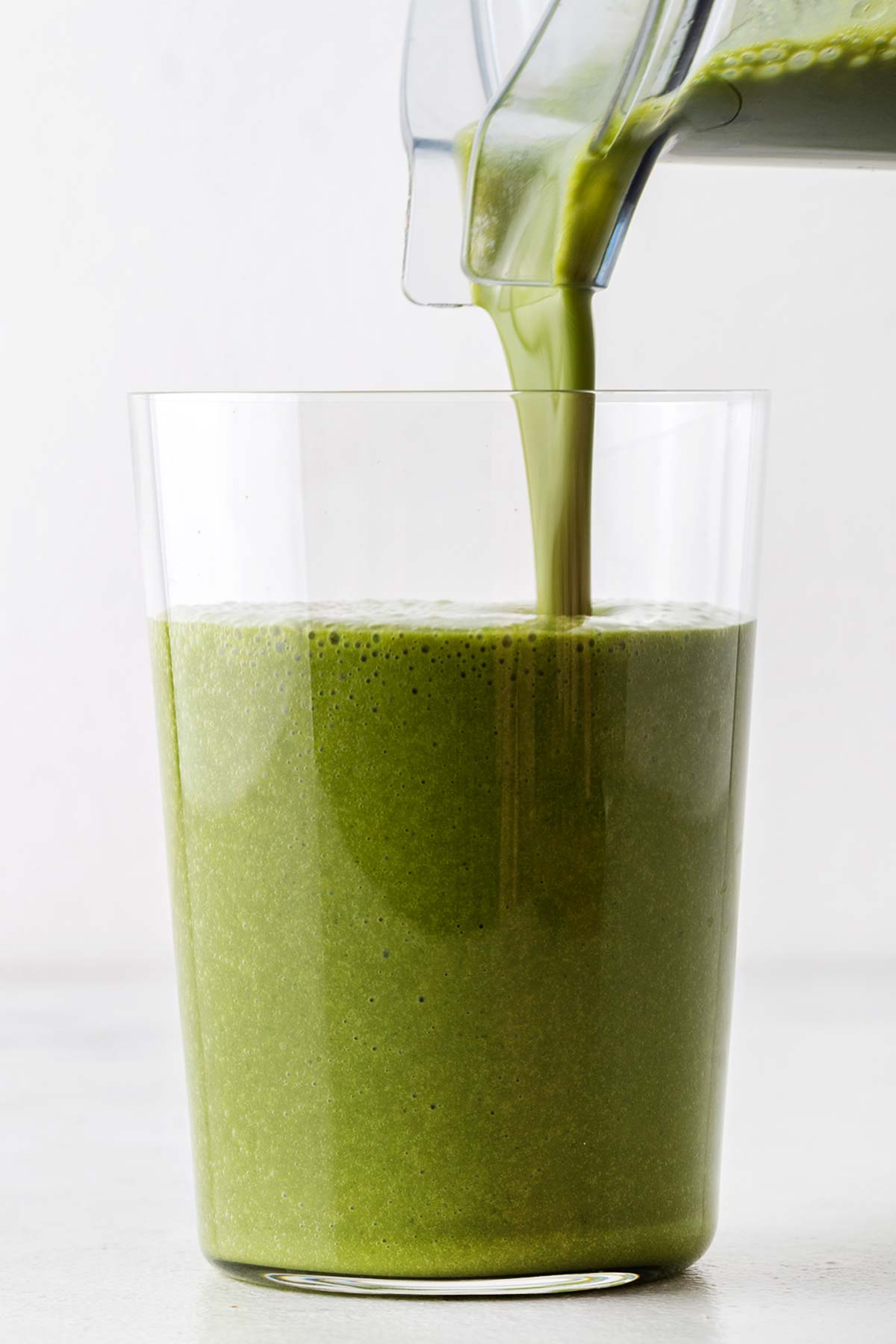 Pouring a matcha smoothie in a glass.