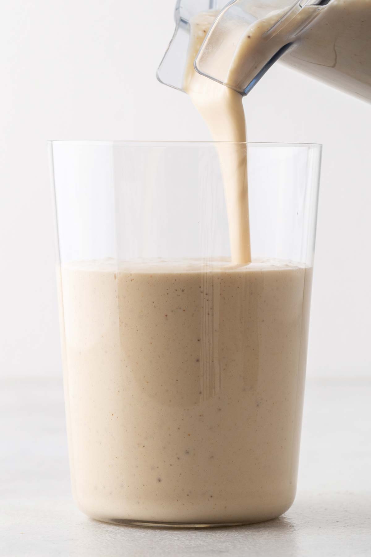 Pouring a peanut butter banana smoothie in a glass.