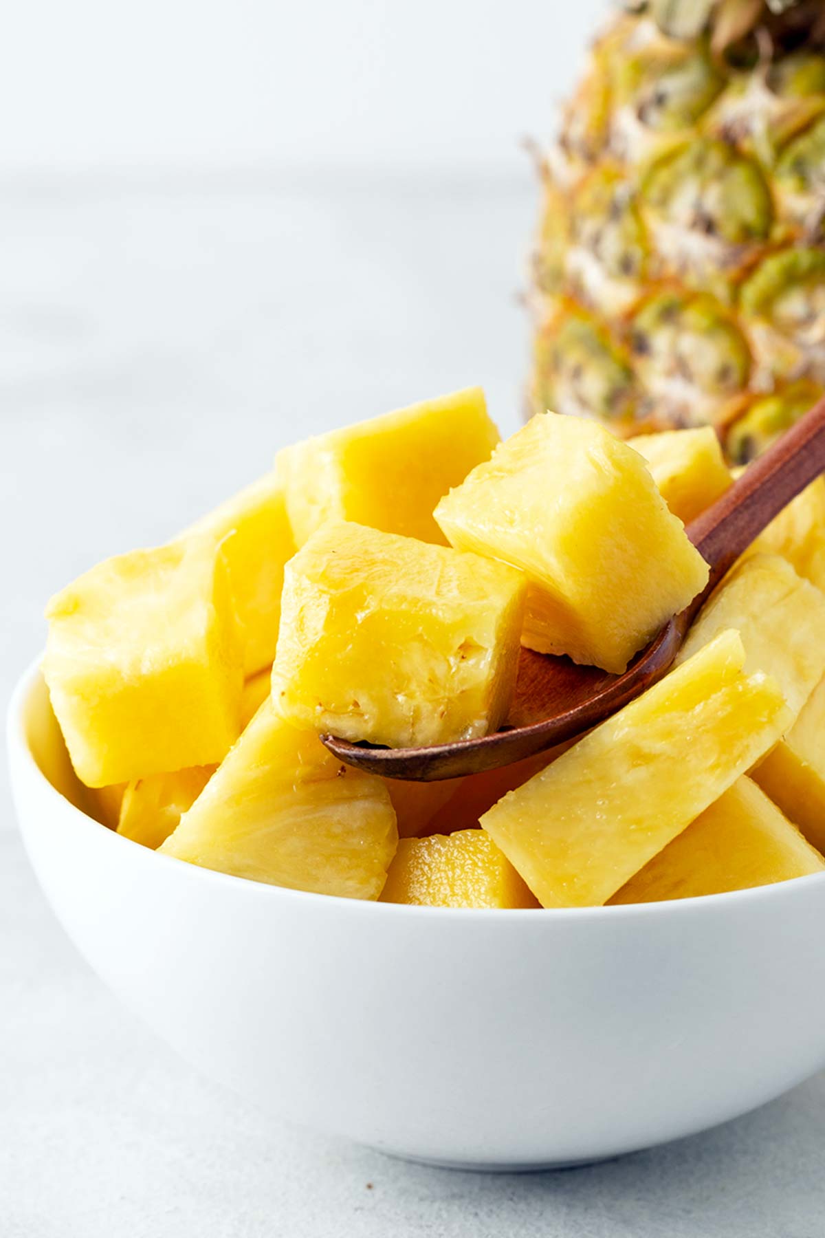 Pineapple chunks in a white bowl with a wooden spoon.
