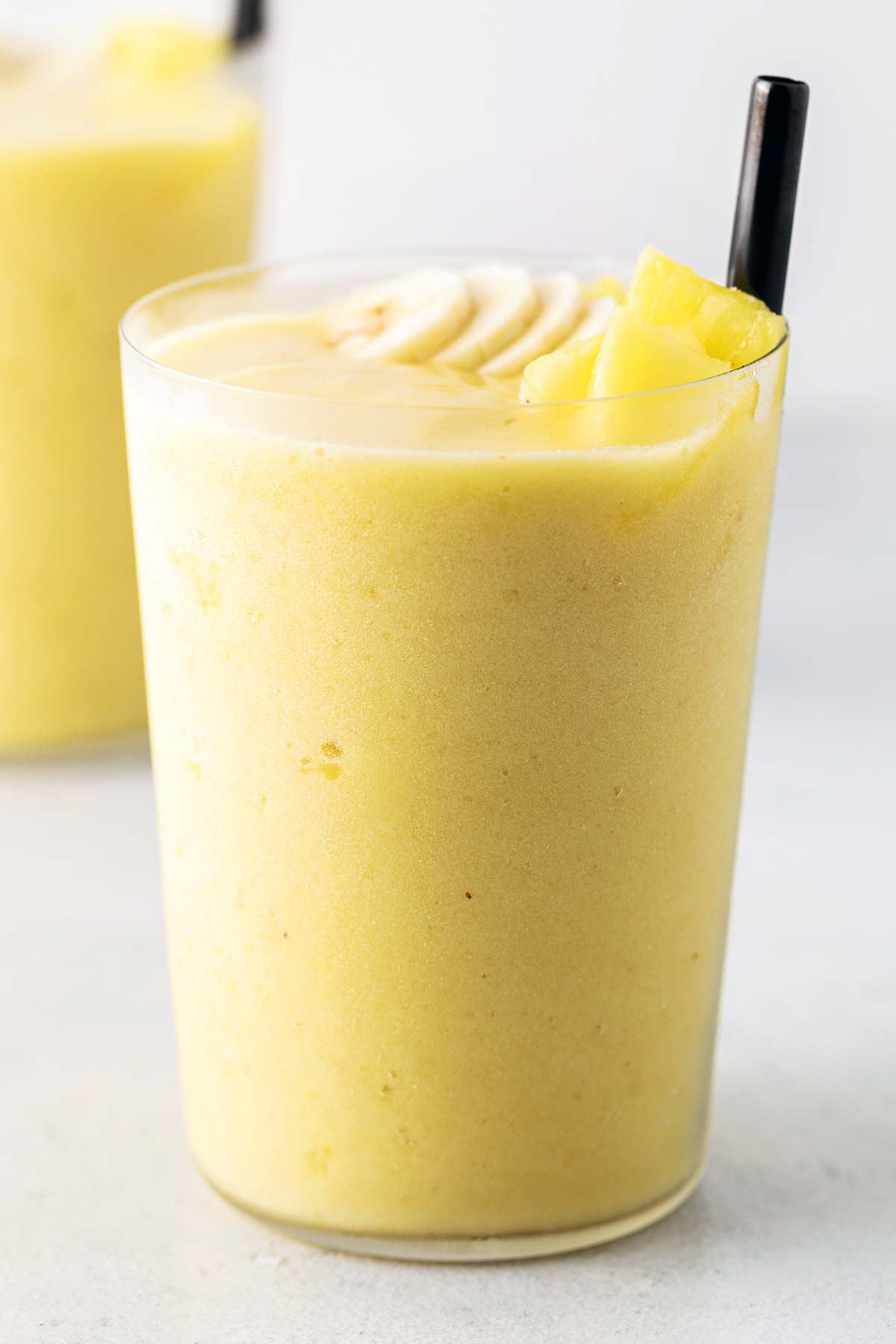 Pineapple smoothie in a tall glass with black straw.
