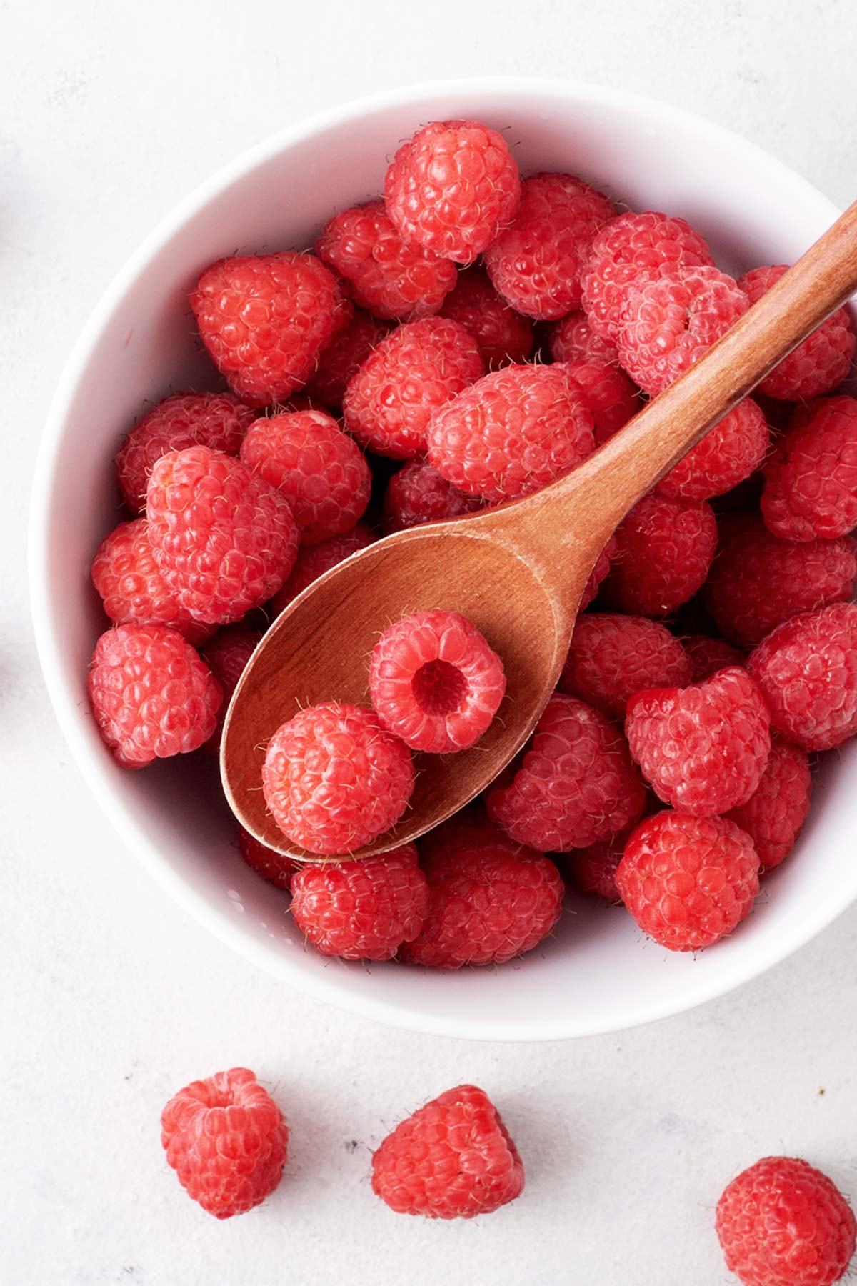 Fresh raspberries in a bowl with a wooden spoon.