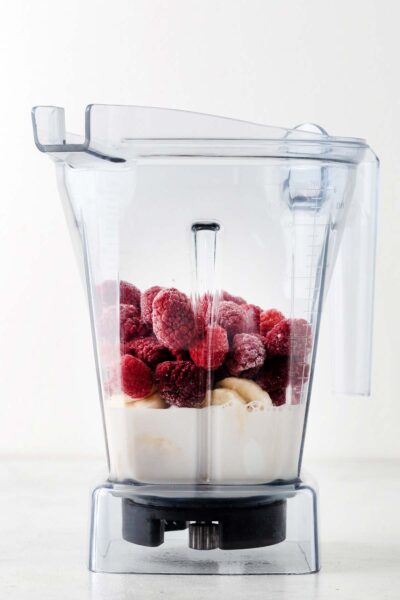Frozen raspberries, banana, and milk in a blender.