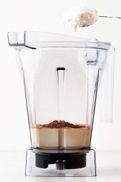 Marshmallow puff being put in a blender with cocoa powder and milk.