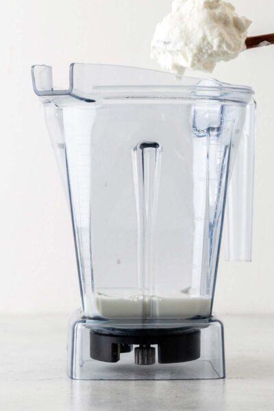 Greek yogurt being put in a blender with milk. 