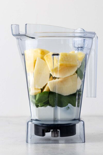 Pineapple, apples, spinach, yogurt, and milk in a blender. 