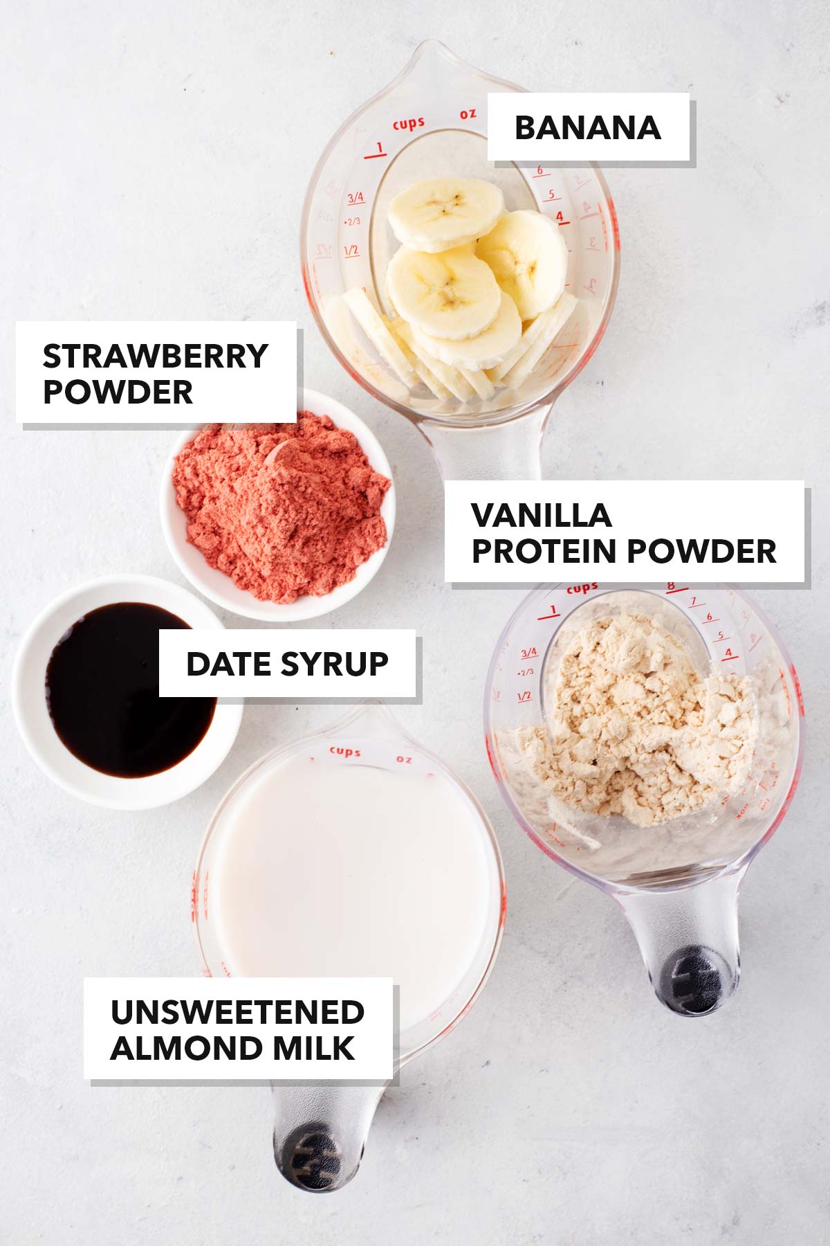 Ingredients for a strawberry banana protein shake on a gray table.