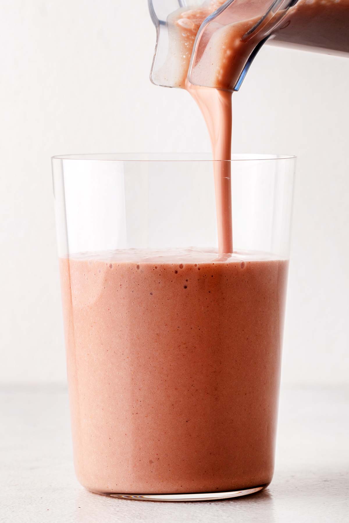 A strawberry banana protein shake being poured into a glass.