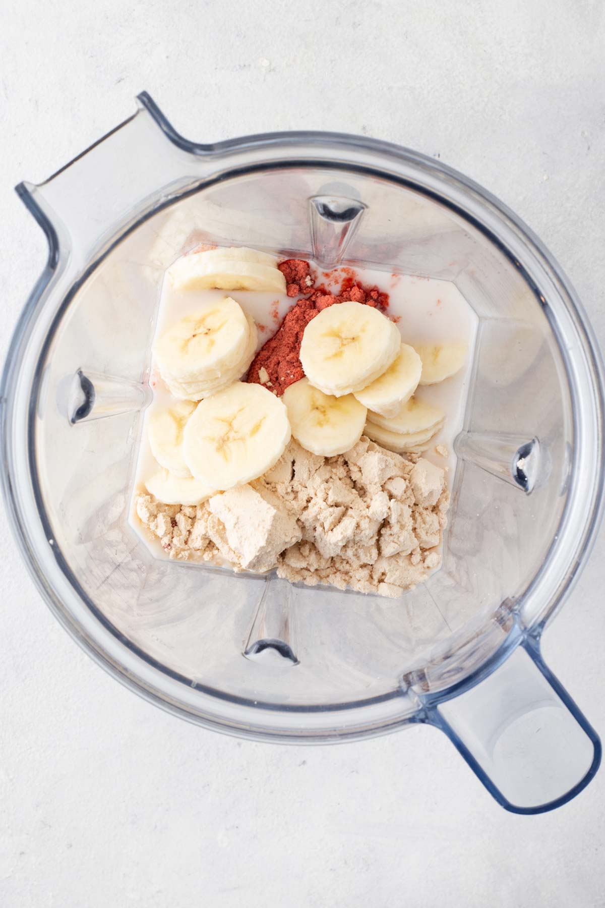 Ingredients for a strawberry banana protein shake in a blender.