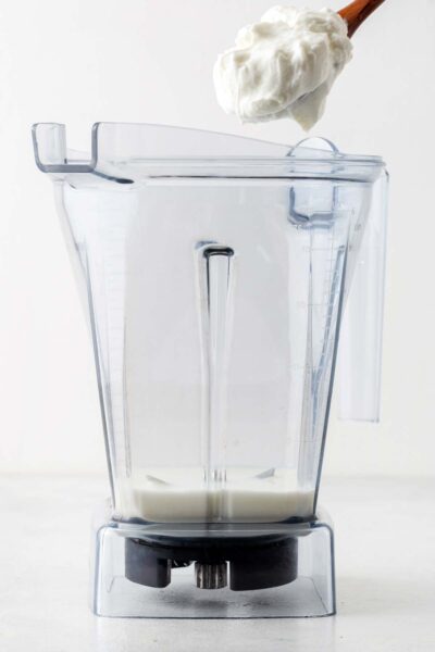 Greek yogurt added to a blender with milk.