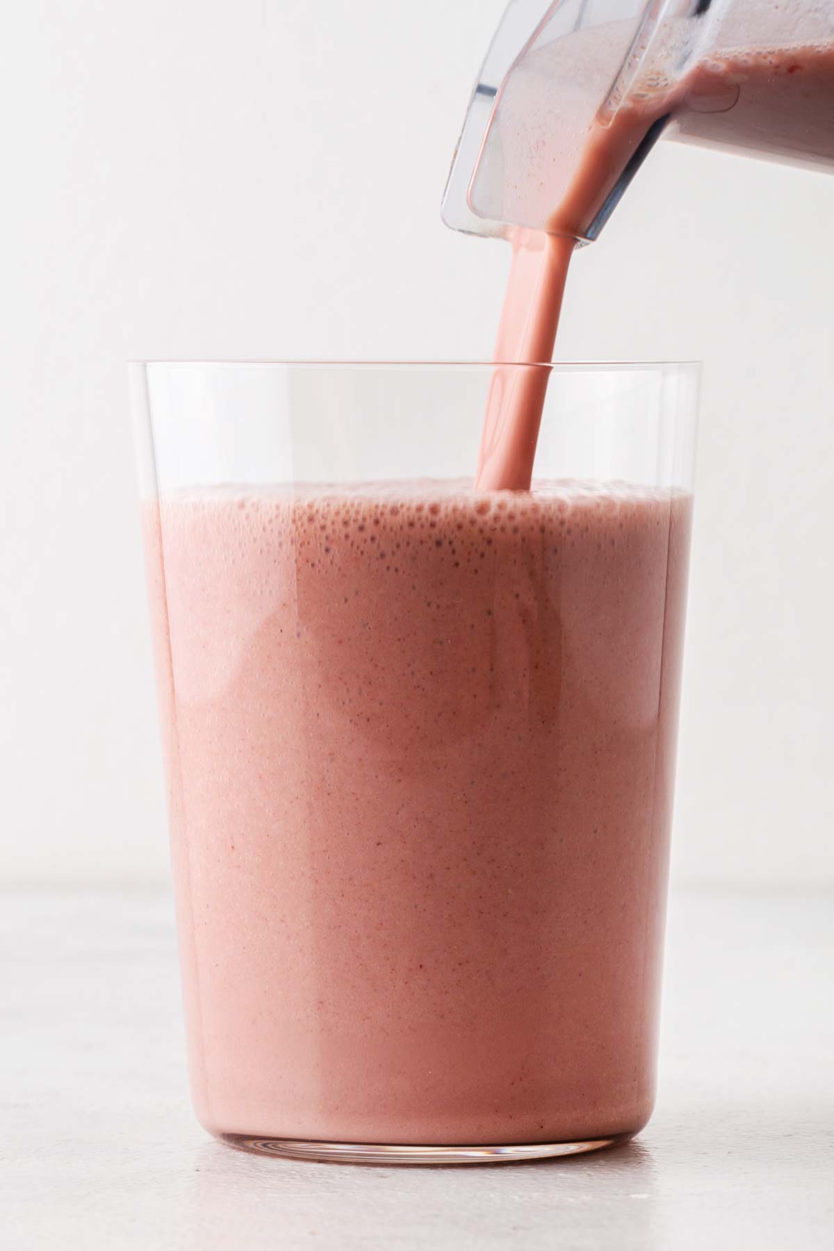 Pouring a strawberry protein shake in a glass.