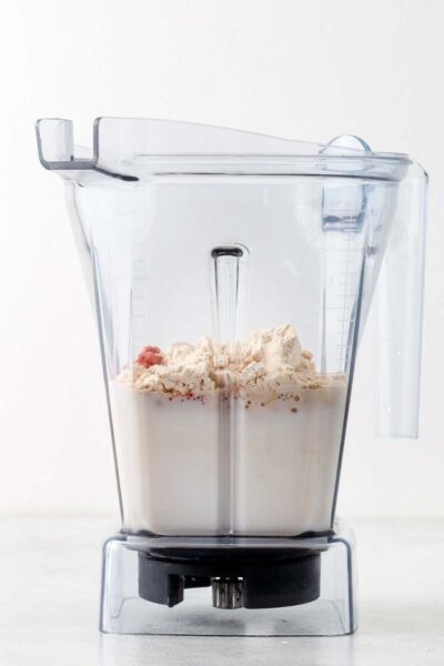 Protein powder, strawberry powder, date syrup, and almond milk in a blender. 
