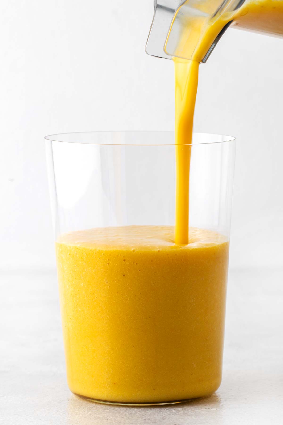 Pouring a turmeric smoothie into a glass.