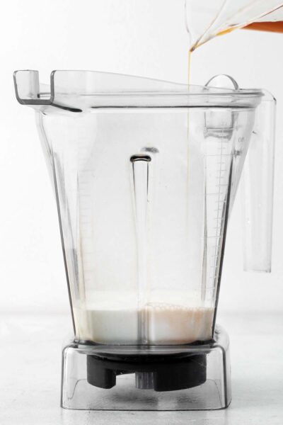 Pouring vanilla extract into a blender with milk.