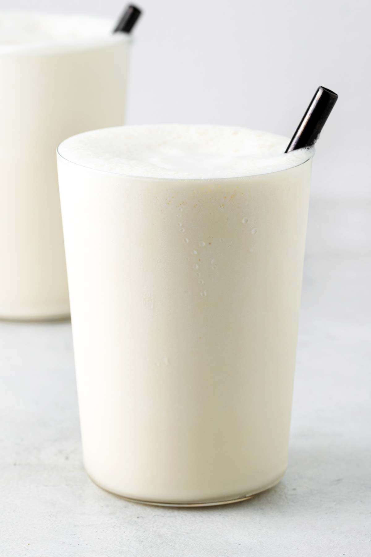 Vanilla milkshake in cups with black straws.